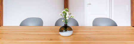 Panorama photo, a glass vase of flowers placed on wooden table with modern gray chairs, interior design of cozy dining room with light pastel wall and doorの写真素材