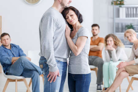 Middle-aged woman embracing tall man during couples therapy in group