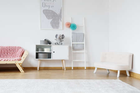 Stylish white settee for kids with grey poster on white wall in designed pastel roomの写真素材