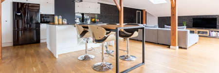 Contemporary black and white open loft space with kitchen, dining room and living area, wooden floor, black brick accents and modern furnitureの写真素材