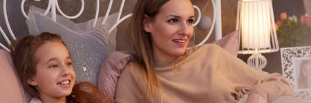 Happy young daughter and her mum watching movies in bedの写真素材