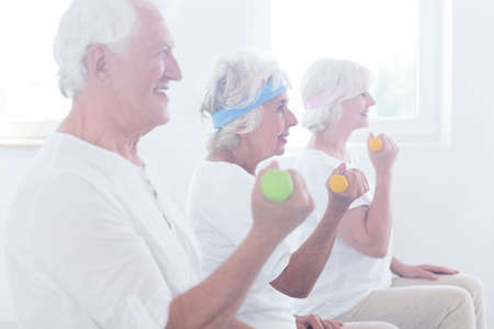 Smiling elderly people lifting colorful dumbbells during fitness classes in studioの写真素材
