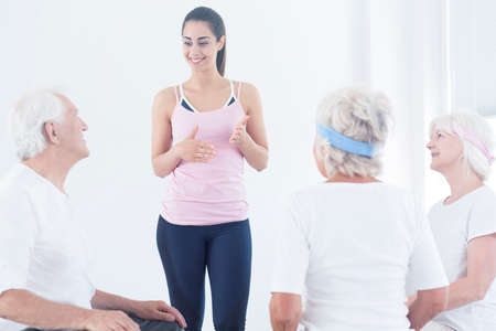 Pretty instructor explaining and describing how to do exercises before training with elderly people