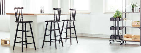 Stylish design of white open space interior for minimalist with wooden kitchen island countertop, retro barstools and vintage accessoriesの写真素材