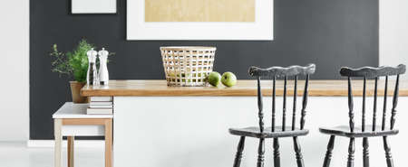 Panorama view of minimalist modern kitchen with black vintage bar chairs standing at white and wooden kitchen island with basket, spices and fresh herbsの写真素材