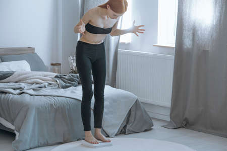 Young undersized woman obsessing over her weight while standing on a scale