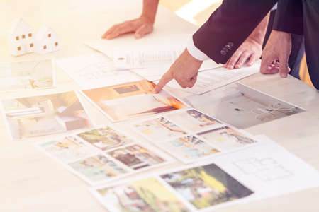 Close-up of people looking at offers of houses for sale while standing at desk with leaflets