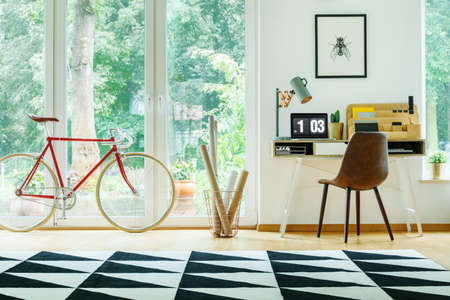 Red bicycle and black chair at desk with laptop and lamp in open work area with view on terrace