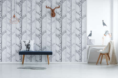 Spacious room with stool against creative wallpaper and white chair with blanket at deskの写真素材