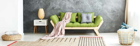 Grey pillow on pouf and pattern carpet in simple living room with green sofa against textured wallの写真素材