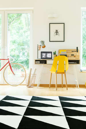 Black and white geometric carpet in spacious workspace with yellow chair at desk with designer lampの写真素材