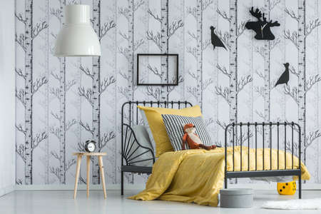 Lamp above stool with clock in white kid's bedroom with red fox toy on bed with pattern pillow