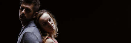 Romantic couple standing back to back against black background