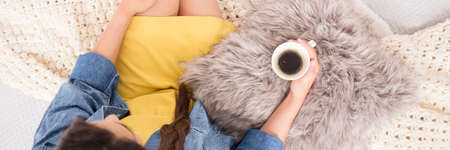 Fashionably dressed blogger sitting on bed, drinking coffee and relaxing after workの写真素材