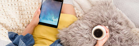 High angle of teenage girl sitting in bed, drinking coffee and watching a movie on tabletの写真素材