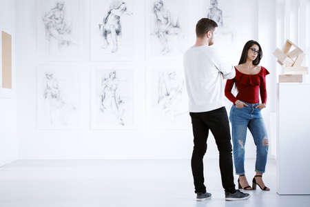 Young couple watching sculpture in bright art center with drawings collection on wallの写真素材