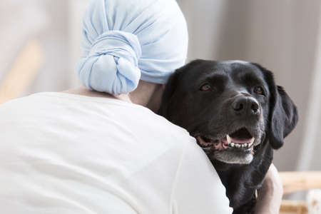 Close-up of patient with cancer hugging black dog during animal assisted therapy