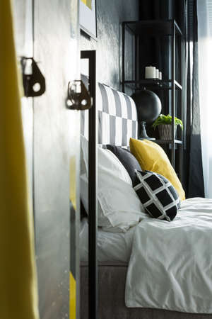 Side angle of metal shelf in bedroom with black, white and yellow pillow on bedの写真素材
