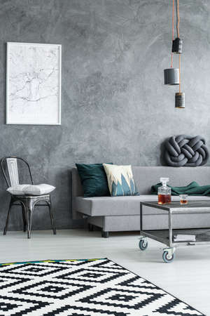 Simple framed poster hanging on grey raw wall in dark living room of bachelor's apartmentの写真素材