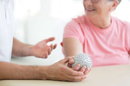 Nursing home patient doing active pnf exercises with a grey spiked ball used for rehabilitation purposesの写真素材