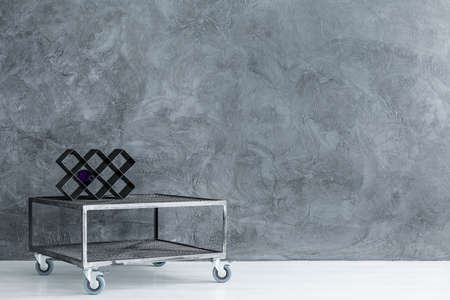 Handmade wine rack with bottle placed on small table with wheels in room with empty wallの写真素材