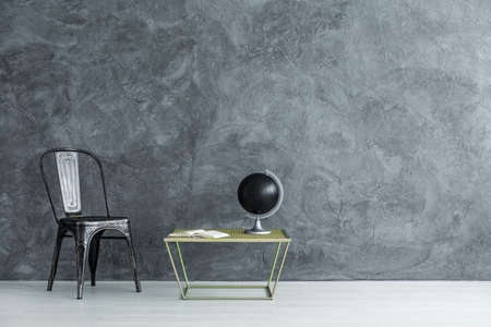 Black globe standing on small table by the copper chair in room with empty wallの写真素材