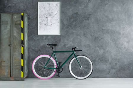 Handmade hipster bicycle standing next to old metal locker in empty walled room with poster
