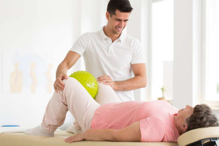 Patient squeezing a green massage ball with her knees while lying on her back