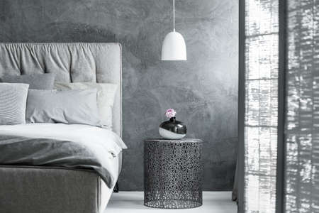 Black and white vase with bright flower on metal designer table in modern bedroom with screenの写真素材