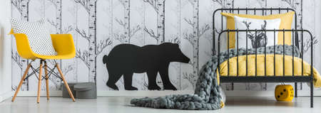 Grey blanket on yellow bed and pillow on yellow chair in kid's bedroom with bear sticker on wallの写真素材