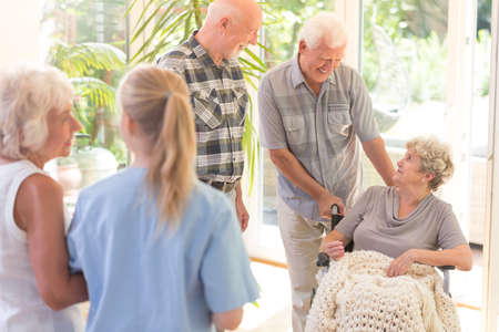 Two elder men visiting their disabled sister in wheelchair at the nursing house