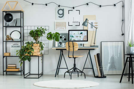 Designer's workspace with classic chair at desk and small tree in wooden container on shelfの写真素材