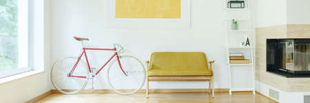 White and red bicycle standing next to yellow sofa in room with fireplace