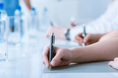 Close-up photo of people making notes with the use of pen during a conference meeting