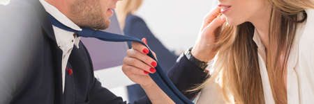 Beautiful woman with red nails touching blue tie of a handsome manの写真素材
