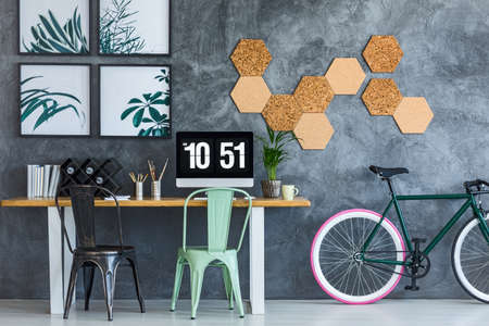 Mint and black chair at table with computer monitor in designer workspace with green bike and corks on the wallの写真素材