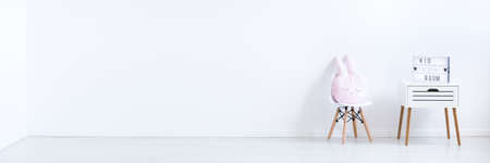 Cute rabbit shaped pink pillow placed on the chair standing next to wooden cupboardの写真素材