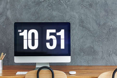 Time display on desktop of computer monitor on wooden desk against concrete wallの写真素材