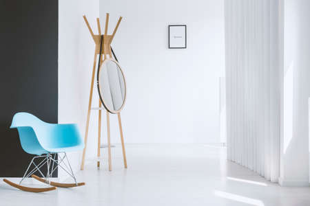 Minimalist white hall of modern apartment with blue rocking chair standing near a black contrasting wallの写真素材