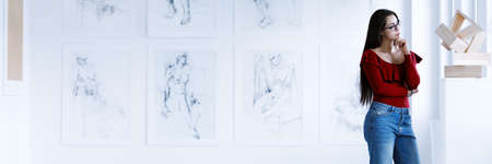Art gallery concept with copy space, young woman wearing casual clothes gazing at modern sculpture standing against wall gallery of drawings in art museumの写真素材