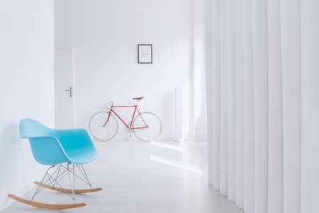 Blue rocking chair and red bicycle standing in simple hall with open entrance doorの写真素材