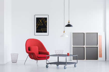 Two black and white lampshades hanging in bright living room with wheeled table and red armchairの写真素材