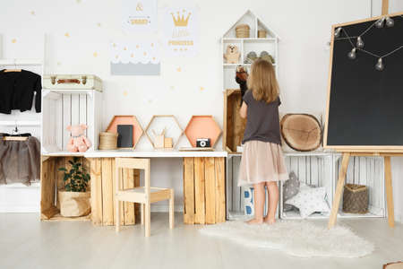 Wooden chair at DIY desk with toys in girl's room with clothes and chalkboardの写真素材