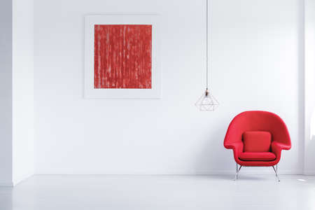 Simple empty room with abstract poster, red armchair and copper lampshadeの写真素材