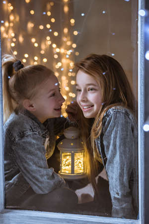 Two sisters sitting on the windowsill at nightの写真素材