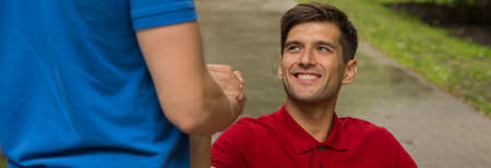 Smiling cheerful man on a wheelchair shaking his friend's helpful handの写真素材