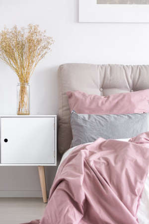 Glass vase with flowers on white wooden chest of drawers in scandinavian bedroom interior with gray and pink decorの写真素材