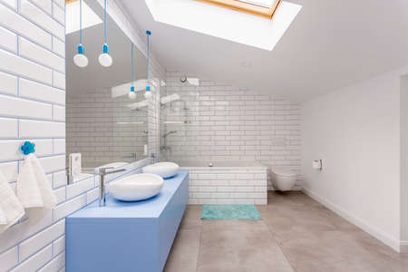 Simple bathroom in the attic with blue washbasin cabinet, toilet and bathtub against white brick...