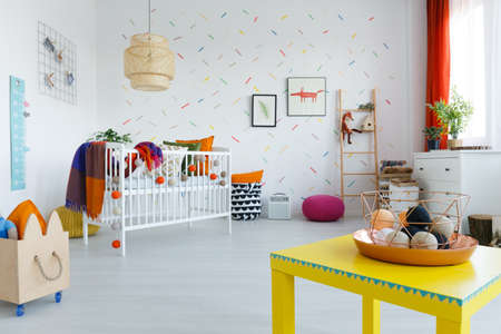 Small balls in copper basket on yellow table in colorful kid's room with wooden box and blanket on bedの写真素材