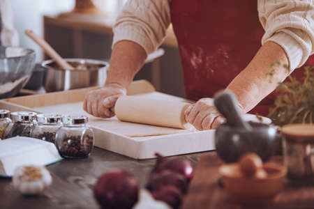 Close-up of senior person rolling out dough on countertop with kitchen toolsの写真素材